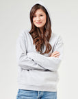 Frau trägt grau melangen Unisex Hoodie aus Bio-Baumwolle mit Kapuze und Kängurutasche. Stylische Kombination mit blauen Jeans für Casual Outfits und umweltfreundliche Streetwear.