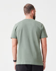Rückansicht eines Mannes der ein Premium TShirt in der Farbe Grün aus Bio-Baumwolle trägt, dazu hat er eine passende schwarze Hose an - nachhaltige Mode für einen lässigen Look.